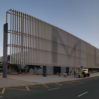 The exterior of Murcia airport's terminal building at dusk, with its slatted facade and passengers waiting at the kerb.
