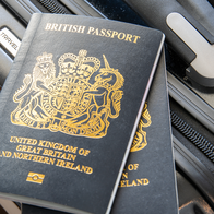 Two dark blue British passports with gold lettering resting on a black suitcase beside its handle.