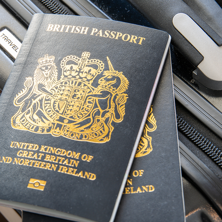 Two dark blue British passports with gold lettering resting on a black suitcase beside its handle.