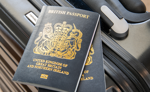 Two dark blue British passports with gold lettering resting on a black suitcase beside its handle.