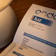 An Endesa electricity bill showing a summary of charges, on a wooden table next to a lit lamp.