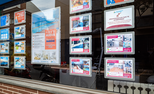 Estate agent's shop window with rows of illuminated panels showing homes for sale, alongside a poster for a new-build development.