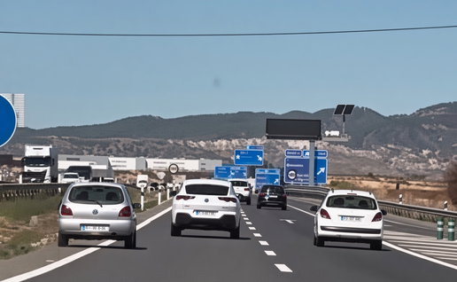 Highway traffic with silver VW Polo, white VW, black car and white hatchback under clear blue sky and road signs.