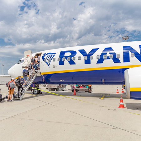 Passengers boarding a Ryanair aircraft via stairs at an airport.