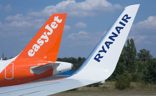 Tail fins of an orange easyJet plane and a white Ryanair plane side by side under a blue sky.