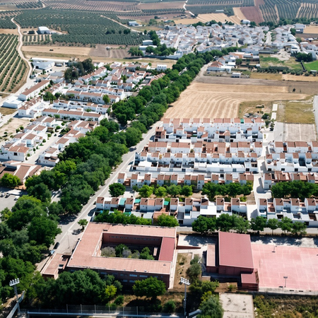 Aerial view of a whitewashed Spanish village with terracotta roofs, olive groves, and surrounding farmland.