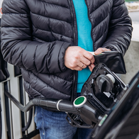 A man holding his wallet open whilst refuelling his car at a petrol station