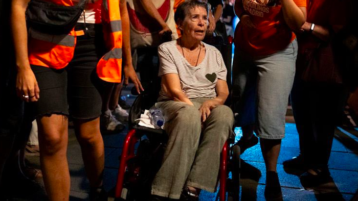 A woman in a wheel chair being pushed along by people wearing reflective jackets