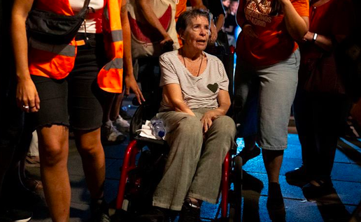 A woman in a wheel chair being pushed along by people wearing reflective jackets