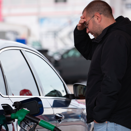 A man rubbing his forehead whilst refuelling his car
