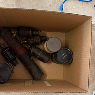 A cardboard box with a selection of hand grenades and mortar rounds inside