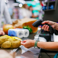 The hand of a cashier at the till scanning the price tag on a bag of potatoes