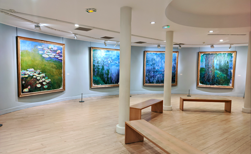 A museum room with paintings of Claude Monet and wooden benches in front of them