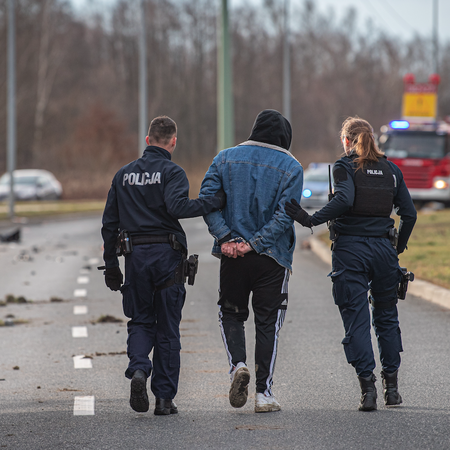 Two police officers escorting a man off of an empty highway