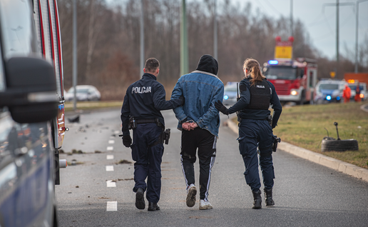 Two police officers escorting a man off of an empty highway