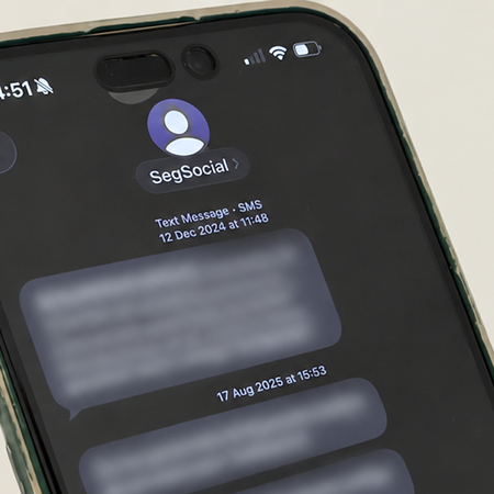 A hand holding a smartphone that shows a text message thread from a sender named SegSocial, with the message text blurred out.