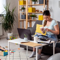 Mother reviewing household bills and paperwork at home while her young child plays nearby.