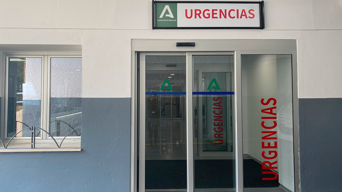 Entrance to a hospital emergency department with a green and white Junta de Andalucía “Urgencias” sign above sliding glass doors.