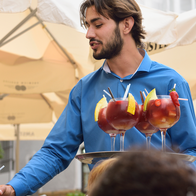 A waiter in a blue shirt serves glasses of sangria to customers at a café terrace.