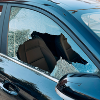 Black SUV parked on a street with its front side window smashed, broken glass around the frame and the leather seat visible inside.