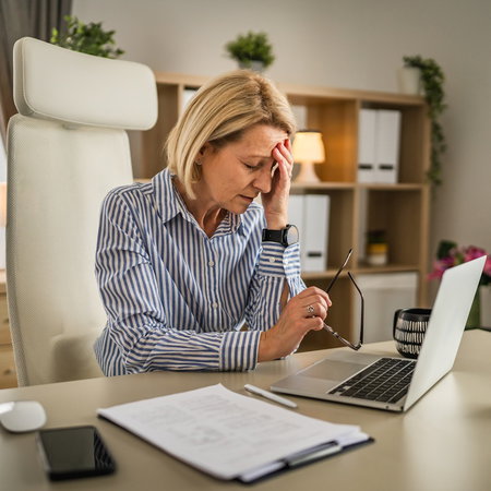 Middle-aged woman holding her forehead while working at a laptop