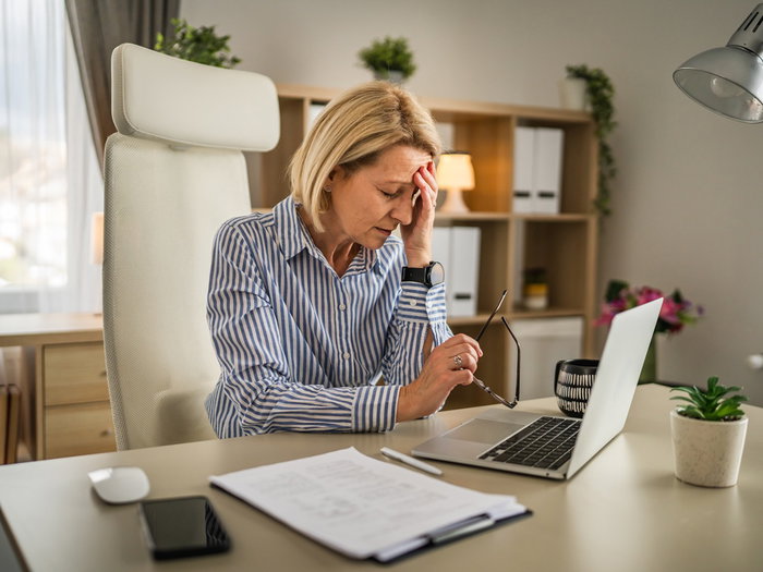 Middle-aged woman holding her forehead while working at a laptop