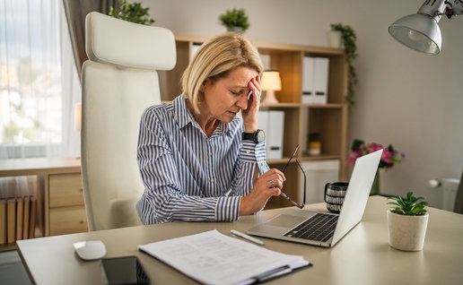 Middle-aged woman holding her forehead while working at a laptop