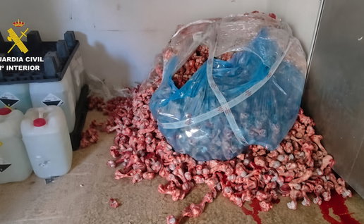 Pile of raw meat scraps and bones on a floor next to chemical containers and a blue plastic bag, with Guardia Civil logo in the top left.