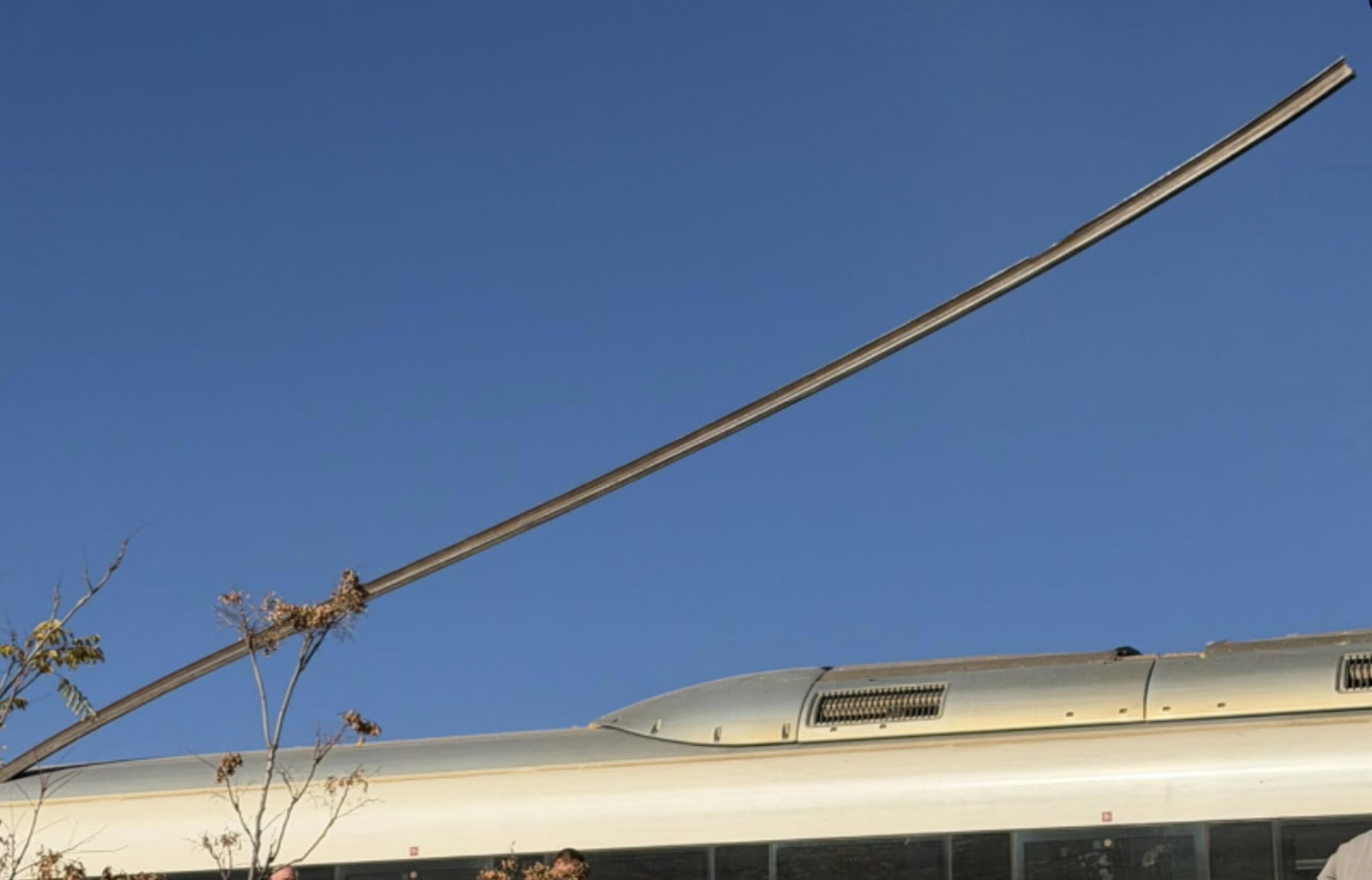 A long rail appears to pierce the roof of a white train carriage beneath a clear blue sky.