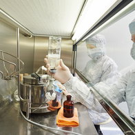 Lab workers in full scrubs managing biohazard material from a confined section of a lab