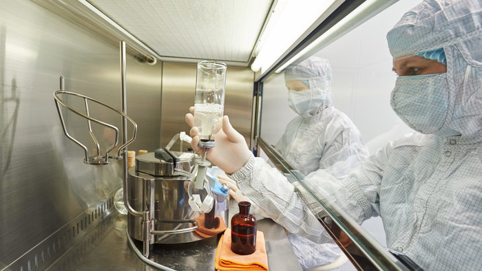 Lab workers in full scrubs managing biohazard material from a confined section of a lab