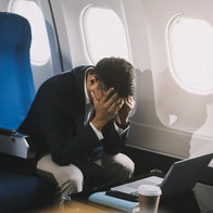 A man sitting in an airplane holding his head in his hands out of fear