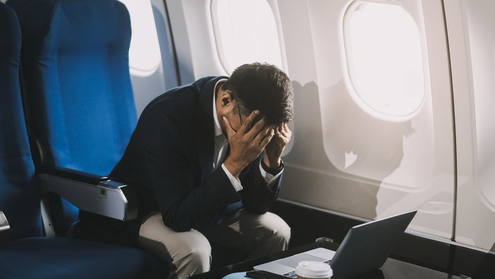A man sitting in an airplane holding his head in his hands out of fear