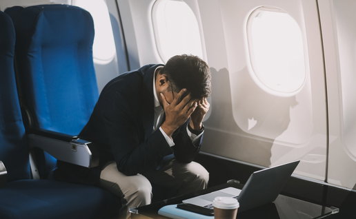 A man sitting in an airplane holding his head in his hands out of fear