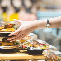 Arm of a young woman reaching out for a container of food in the 'ready made' section.