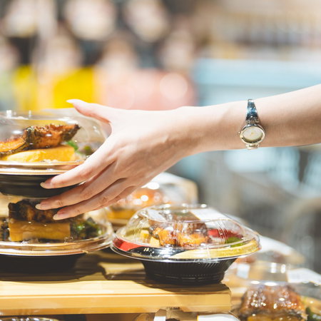 Arm of a young woman reaching out for a container of food in the 'ready made' section.