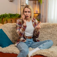 Woman looking surprised while speaking on her mobile phone at home, illustrating unwanted sales calls in Spain.