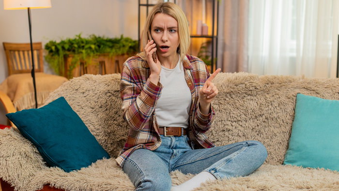 Woman looking surprised while speaking on her mobile phone at home, illustrating unwanted sales calls in Spain.
