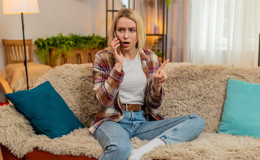 Woman looking surprised while speaking on her mobile phone at home, illustrating unwanted sales calls in Spain.