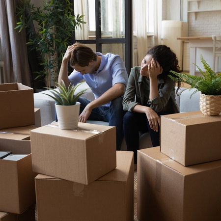 Worried couple sitting among moving boxes, illustrating the impact of eviction proceedings in Spain.