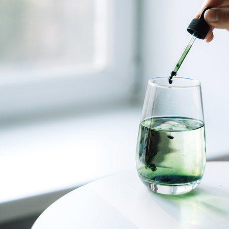 Dropper adding green liquid to a glass, illustrating Spain's recall of a supplement containing undeclared sildenafil.