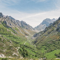 Green mountain valley with scattered stone buildings and winding roads in northern Spain.