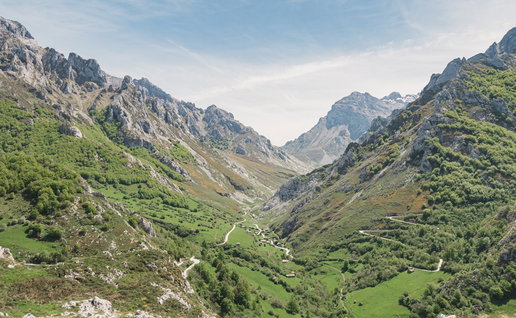 Green mountain valley with scattered stone buildings and winding roads in northern Spain.