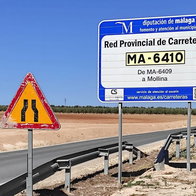 worn out road signs and elderly couple walking along the edge of the road