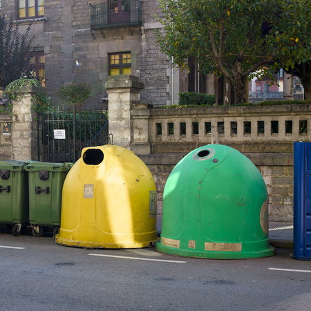 Colourful rubbish and recycling bins lining a street in Spain, illustrating municipal waste collection charges.
