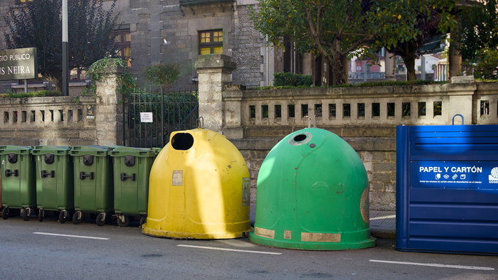 Colourful rubbish and recycling bins lining a street in Spain, illustrating municipal waste collection charges.